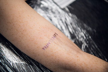 The process of tattooing on a woman's hand inscriptions in French printemps -- spring. Close-up in...