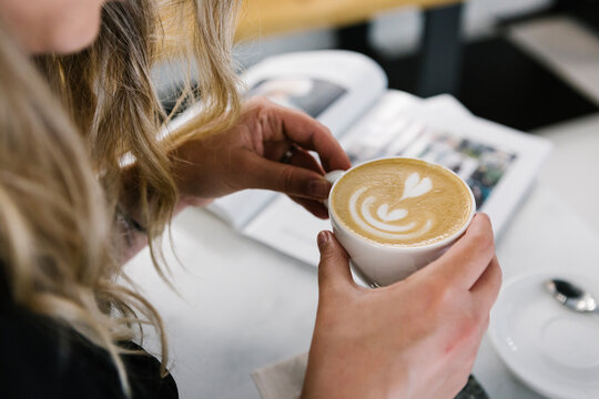 Woman holding cappuccino cup while sitting at coffee shop