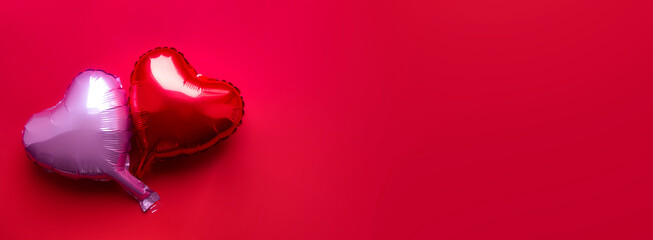 on a red background there are two heart-shaped foil balloons - red and purple