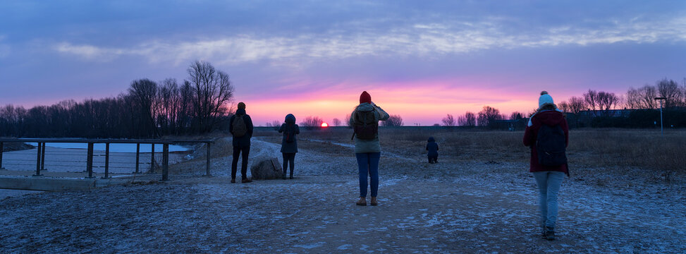 Five Unrecognizable People Seen From Behind Looking At Sunrise At A Winter Dusk In A Frozen Landscape Panorama