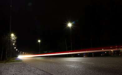 Ray of lights from cars at night. Red and white light shine bright. Lamp post shining damp. Long exposure photo. Järfälla, Stockholm, Sweden.