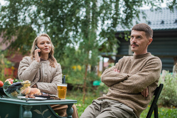 Family social scene. A woman continuously talks on the phone during a family barbecue dinner. The husband shows his dissatisfaction with this situation