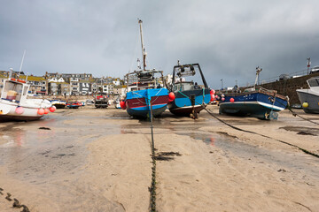Fishing boats beached at low tide in St. Ives' Harbour, Cornwall, UK: rainstorm approaching.