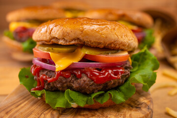 Big tasty burger with beef, tomato, lettuce, red onion, cheese, mustard and ketchup on wooden chopped board with french fries.