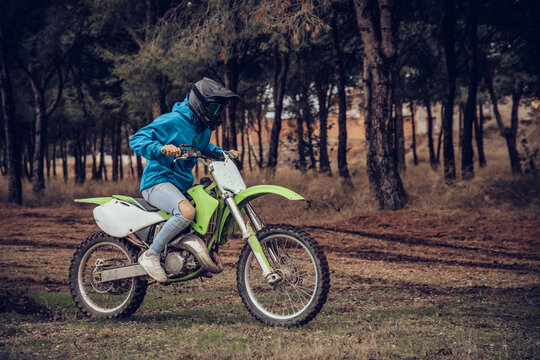 Male teenager riding motorcycle in forest on dirt road during autumn