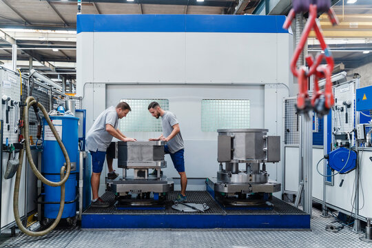 Professional male engineer examining machine while standing at illuminated factory