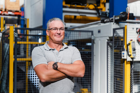 Confident male engineer with arms crossed standing in factory