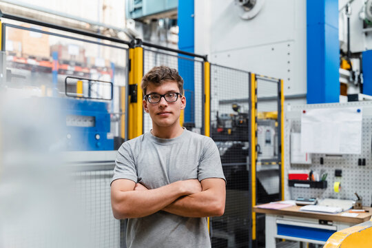Young male worker with arms crossed at illuminated factory