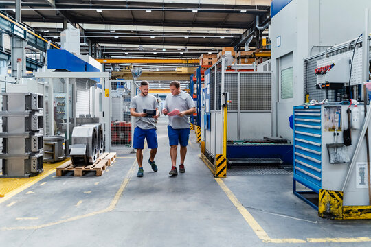 Male manual workers discussing while walking in illuminated factory