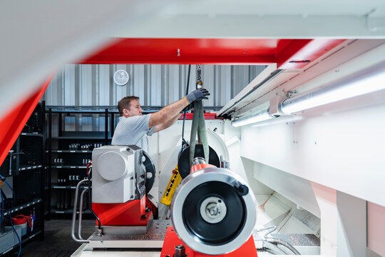 Male technician fastening hook on machine at illuminated modern industry