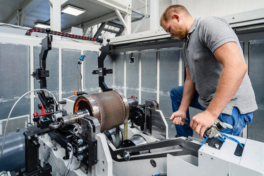 Technician fastening bolts of machine with wrench while standing at factory