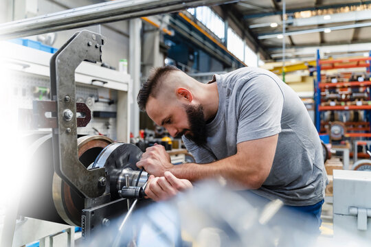 Professional male engineer fastening nut on machine in illuminated industry - Powered by Adobe