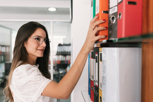Businesswoman taking file from shelf while standing at office