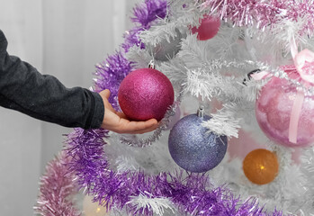 White Christmas tree. Child's hand touches balls on the Christmas tree. Close-up.