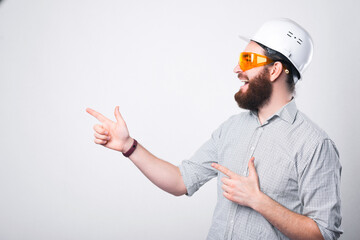 Amazing engineer wearing white helmet and wearing protective glasses pointing at copyspace
