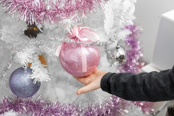 White Christmas tree. Child's hand touches balls on the Christmas tree. Close-up.