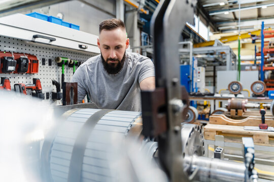Mid adult male engineer analyzing steel machine part in illuminated industry