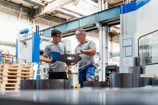 Mature male engineer explaining young colleague about product at industry