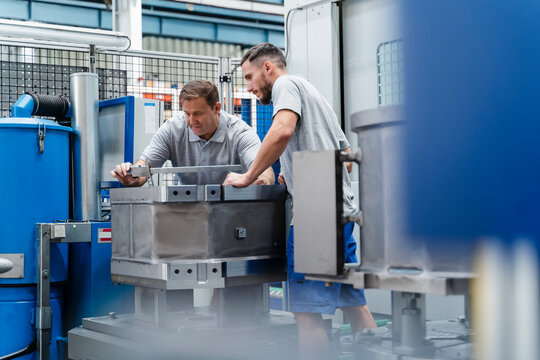 Mature male workers measuring machine at illuminated factory