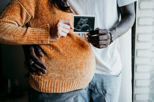 Pregnant woman with young man showing ultrasound scan at home