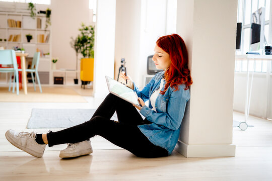 Young businesswoman working on digital tablet while leaning on pillar at office