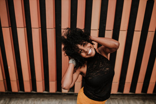 Carefree woman with hand in hair standing against wall