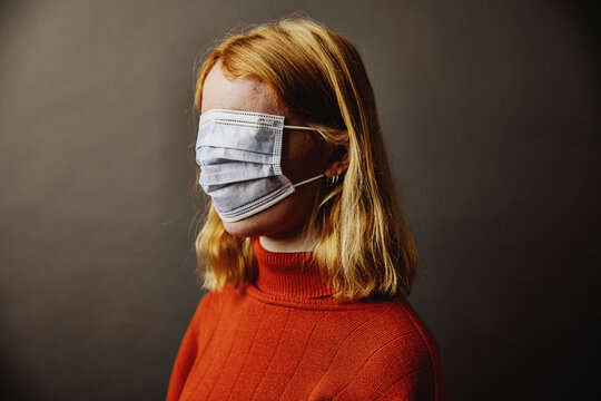 Blond girl wearing protective face mask on face while standing against gray background