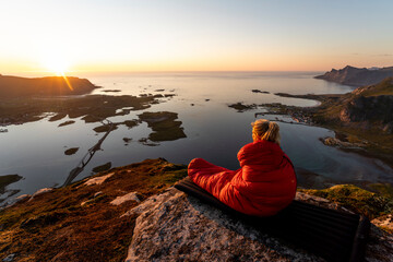 Female hiker wrapped in sleeping bag sitting on mountain at Volandstinden, Lofoten, Norway