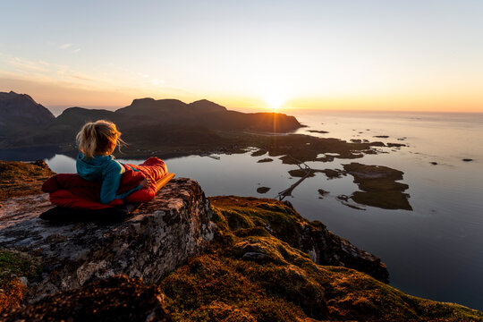 Hiker admiring sunset view while lying in sleeping bag at Volandstinden, Lofoten
