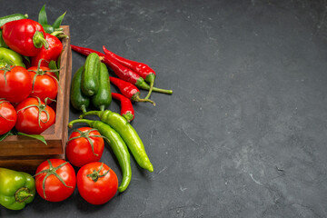 Side view of fresh vegetables inside and outside of a brown wooden basket on the right side on dark background