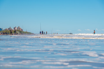 Mar del Tuyú, Buenos Aires, Argentina; December 06, 2020: View of the beach with a lot of fishermen and a pier in the background from inside the water