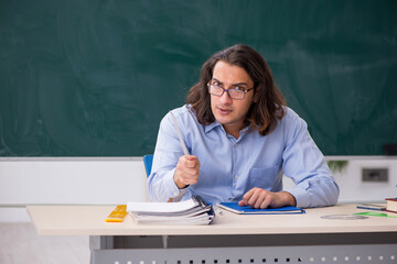 Young male teacher in front of green board