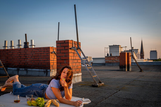 Brunette woman eating fruits, having a rooftop picnic at sunset sunset