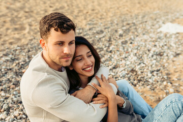 Young couple embracing while sitting on sand at beach