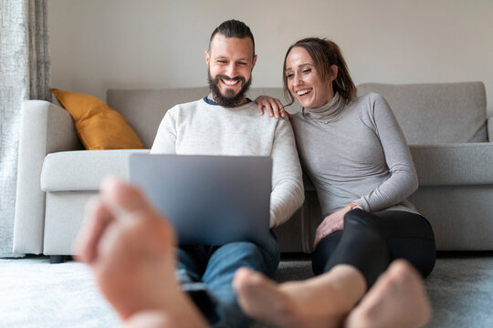 Couple laughing while watching movie on laptop in living room