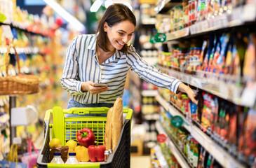 Woman holding smartphone standing in store taking products