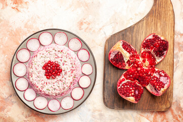 Delicious chicken salad with beet on a gray plate open pomegranate on wooden cutting board on mixed color background