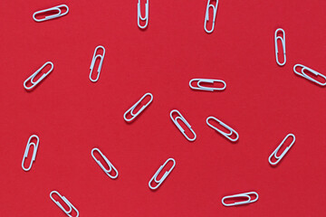 White metal paper clips scattered randomly on a red background. Business concept. Study concept.