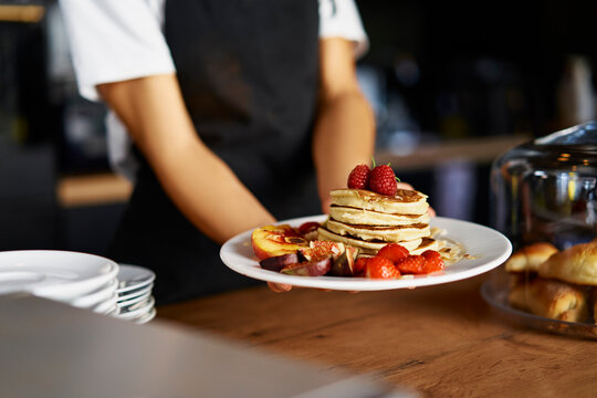 Midsection of female barista holding food plate at cafe