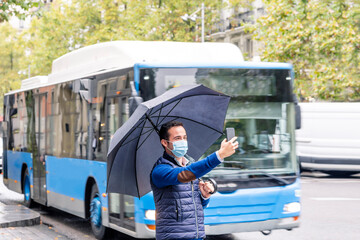 Young man taking selfie with protective face mask and umbrella while standing in city