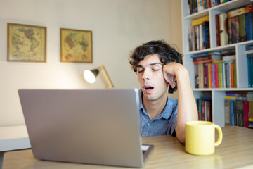 Tired man after working or studying hard on the computer. Young man sleepy from spending the night working or studying hard.