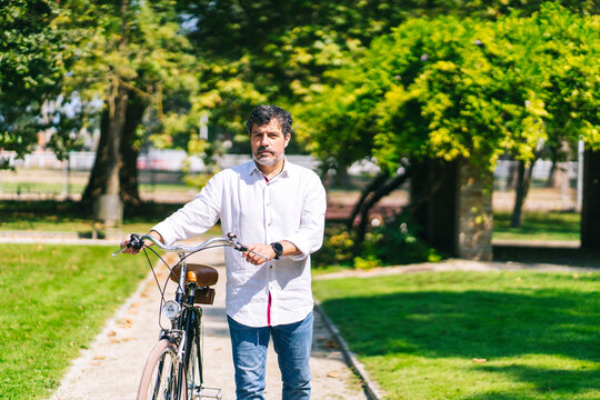 Mature man with bicycle walking on walkway in park on sunny day - Powered by Adobe