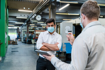 Male entrepreneurs using digital tablet while social distancing in industry