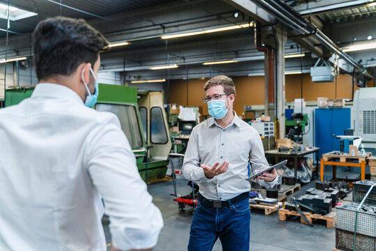 Male entrepreneurs discussing while wearing protective face mask in industry