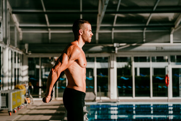 Handsome swimmer doing warm up exercise at poolside