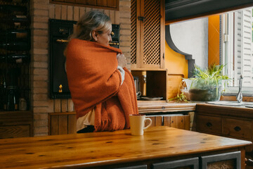 Senior woman covering blanket while standing in kitchen at home