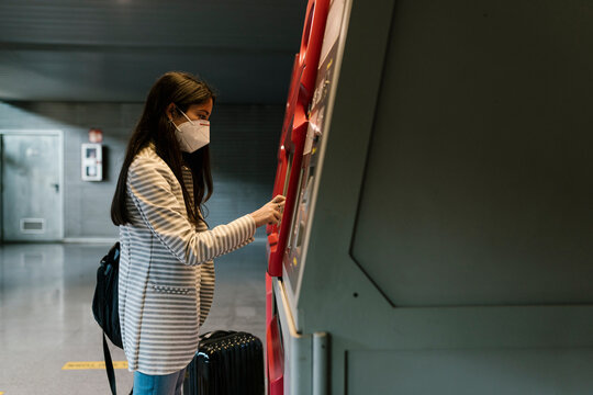 Woman with face mask using kiosk for buying train ticket during COVID-19