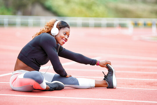 Female athlete listening music while doing stretching exercise sitting on runner track