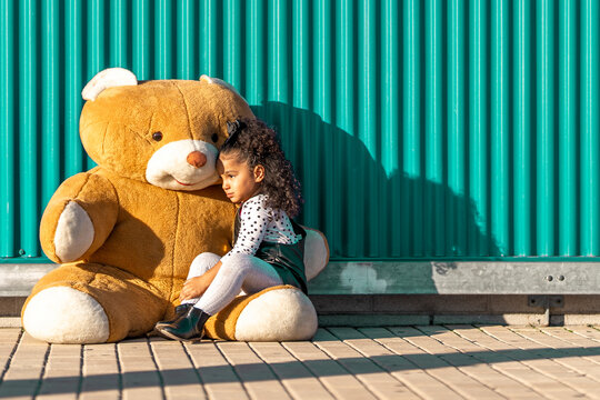 Naklejki Girl embracing while sitting with teddy bear against green wall