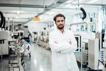 Male scientist wearing lab coat while standing with arms crossed at bright laboratory